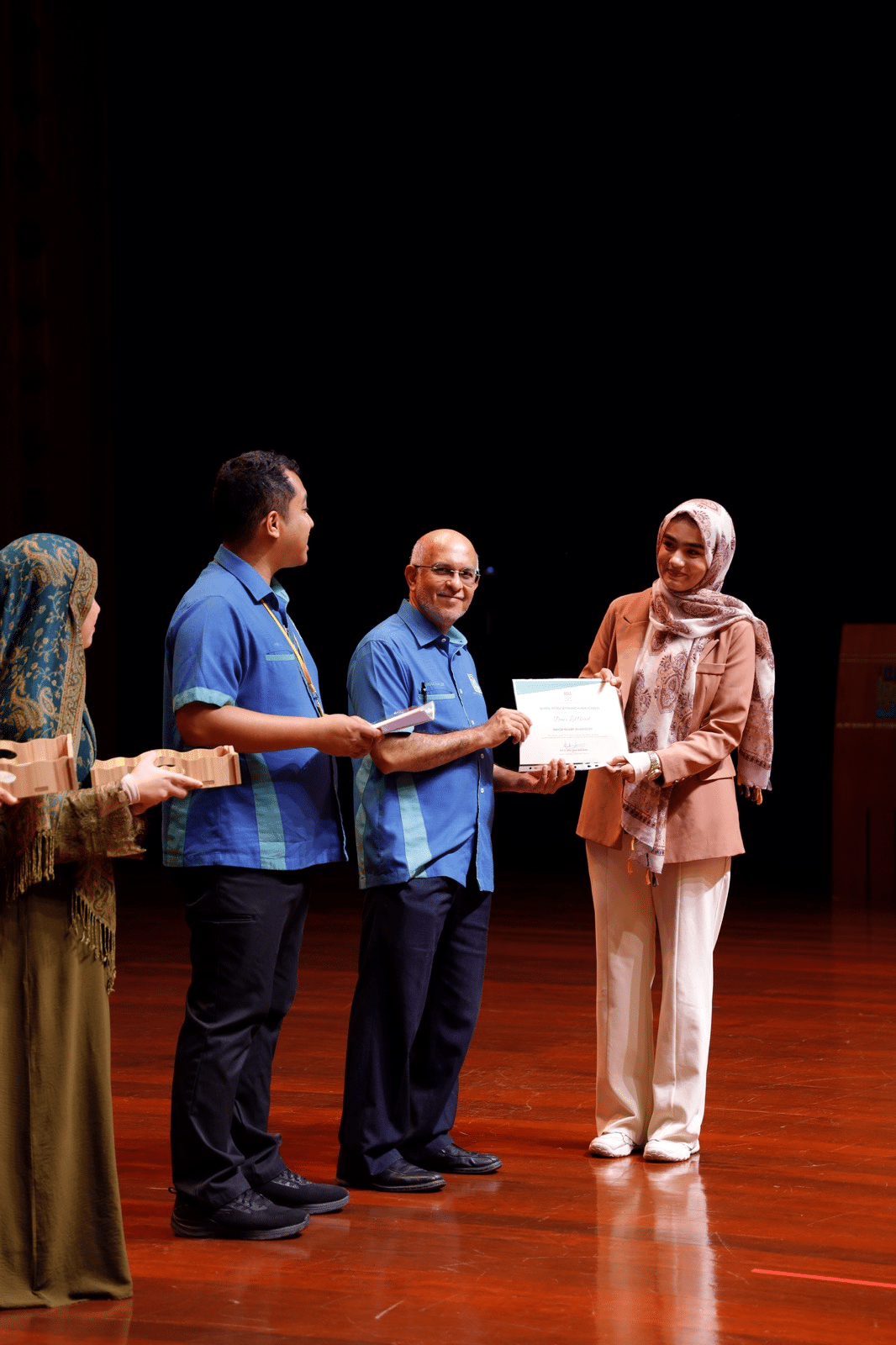 An ASRF student being presented with her Dean’s List certificate on stage by university officials at Albukhary International University
