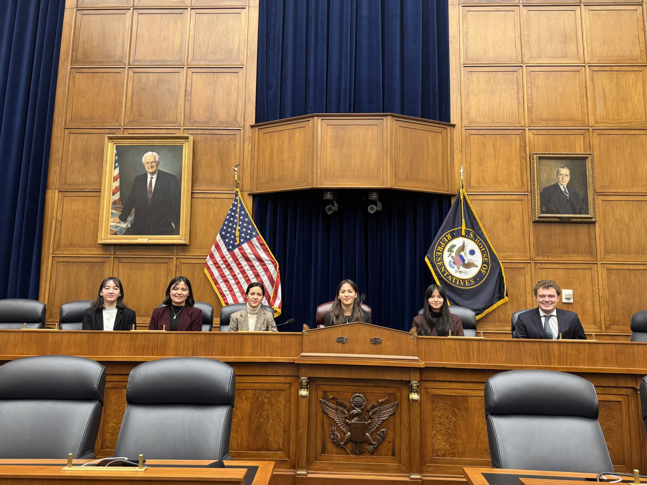 ASRF students seated at the dais of an empty congressional hearing room, beneath the committee seal and a United States flag
