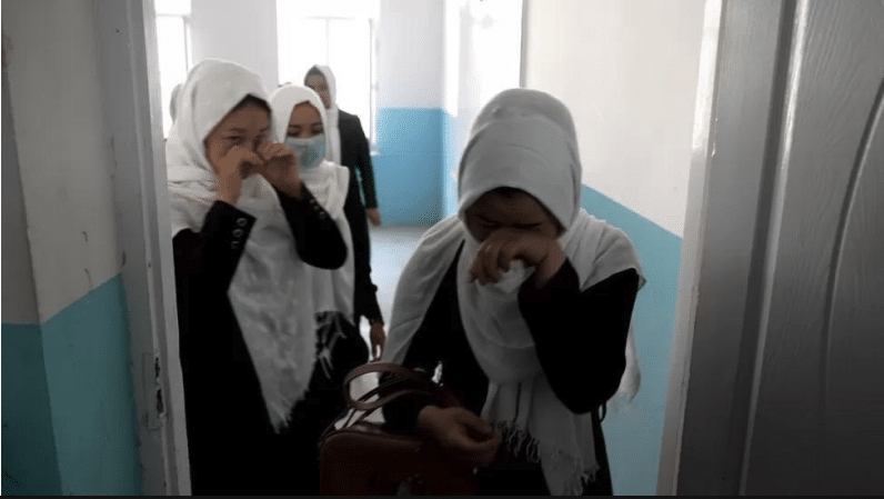 Afghan women in headscarves standing in a corridor, one wiping her eyes