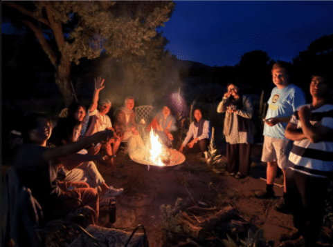 Students and scouts gathered around a campfire at dusk