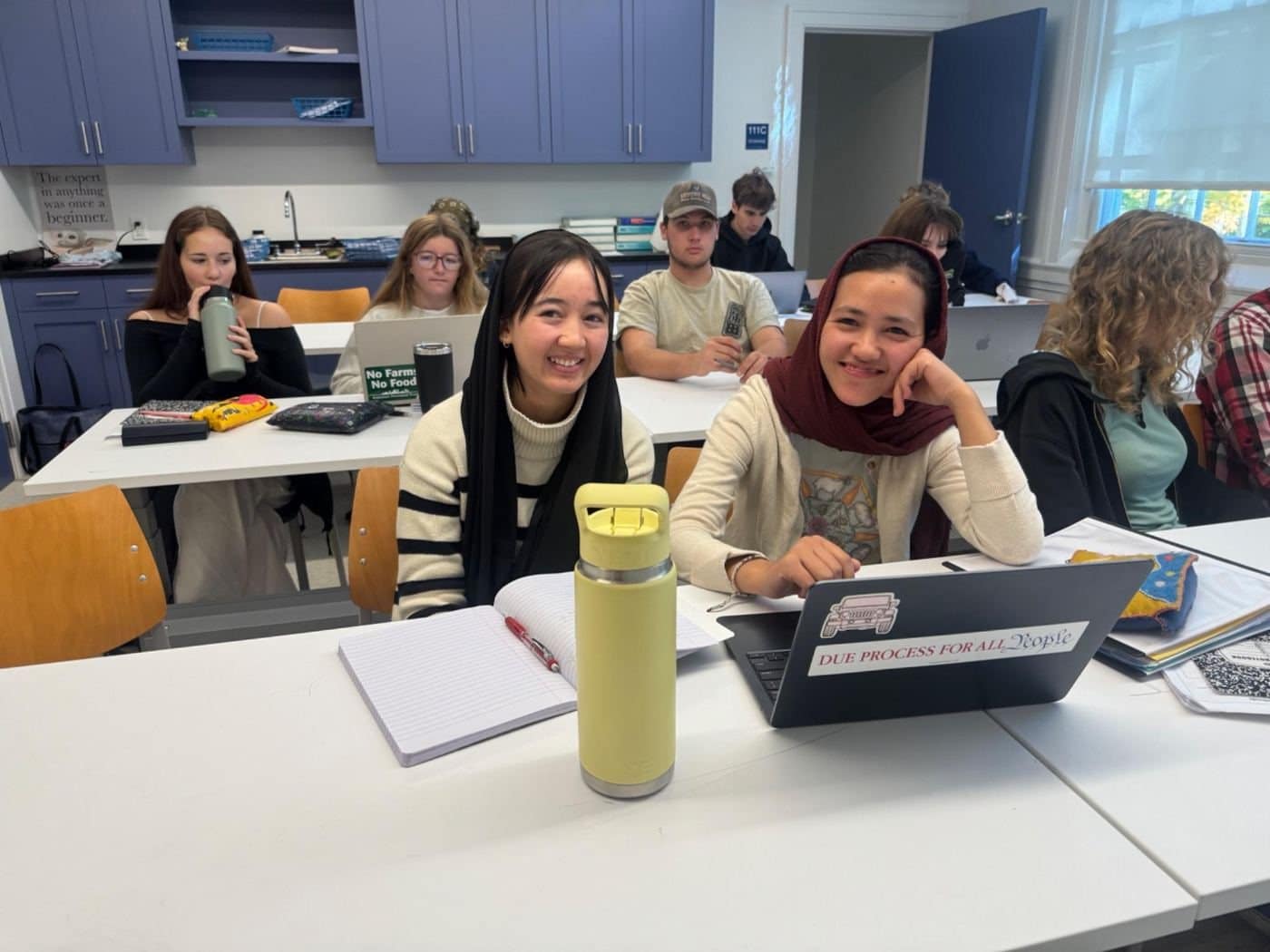 ASRF students sitting together at tables in a bright classroom, laptops and notebooks open in front of them