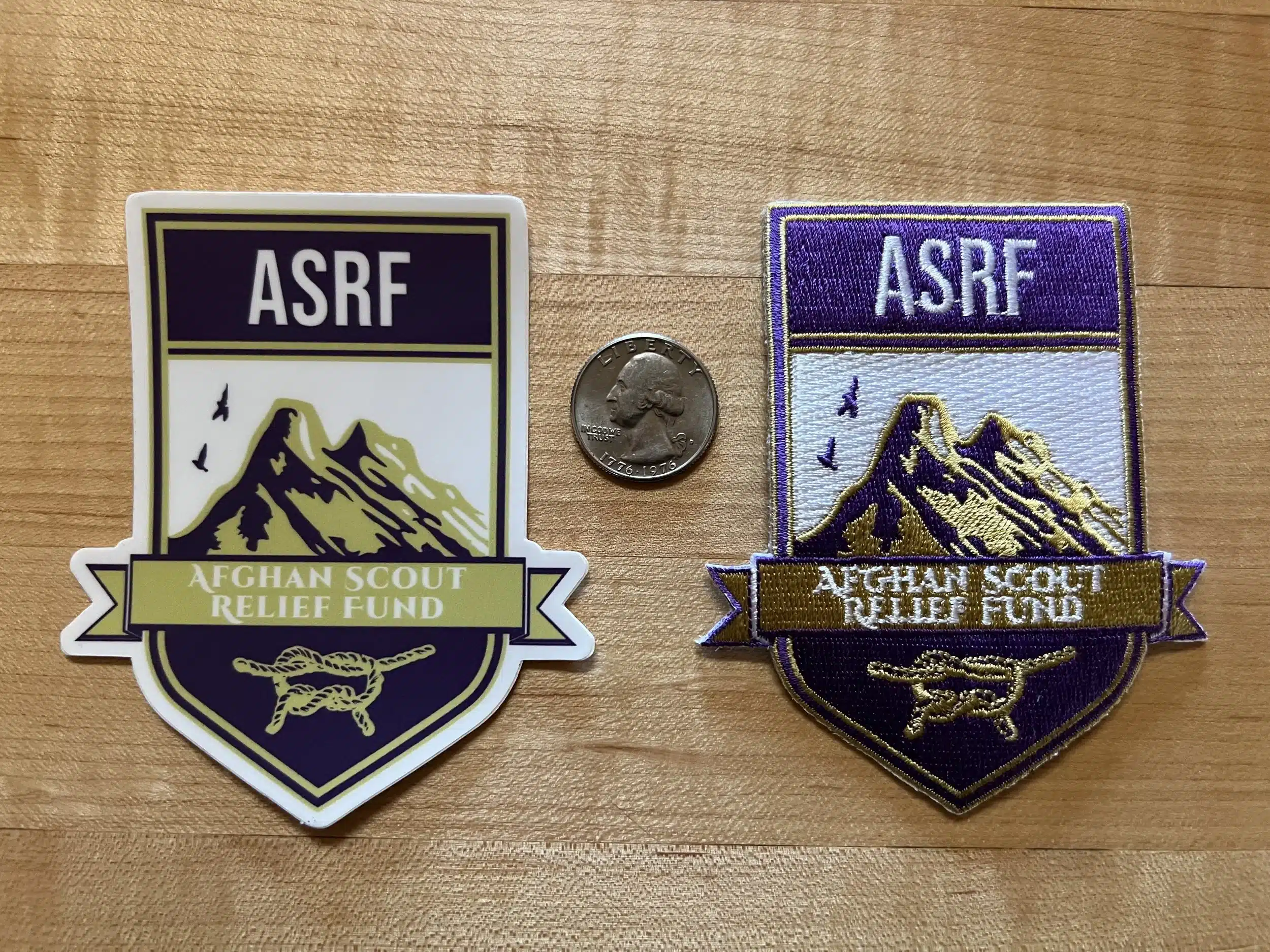 Two embroidered ASRF patches showing a shield with mountains, photographed beside a quarter for scale