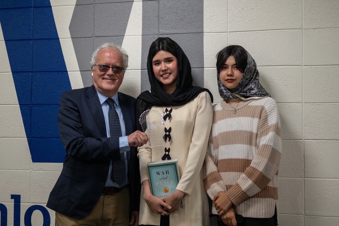 An ASRF supporter standing with two Afghan students at an airport arrivals hall