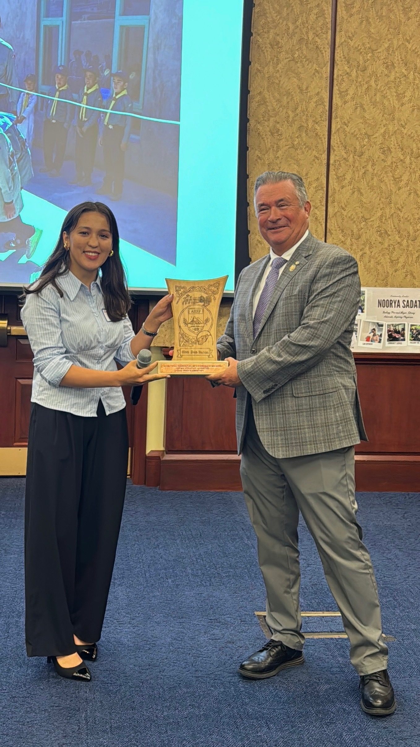 An ASRF student handing an engraved wooden award to Congressman Don Bacon on stage