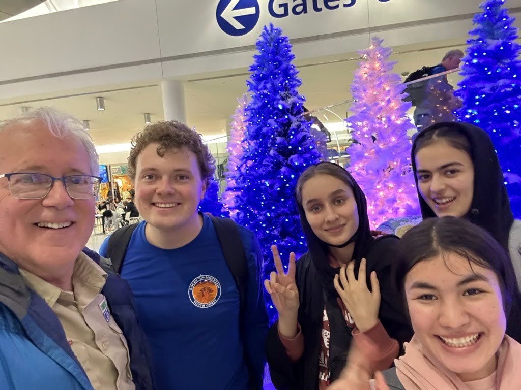 Newly arrived Afghan students with ASRF volunteers beside blue holiday trees at JFK airport