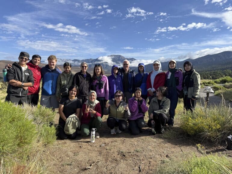 A large group of scouts and volunteers posing together on a hillside with mountains behind them