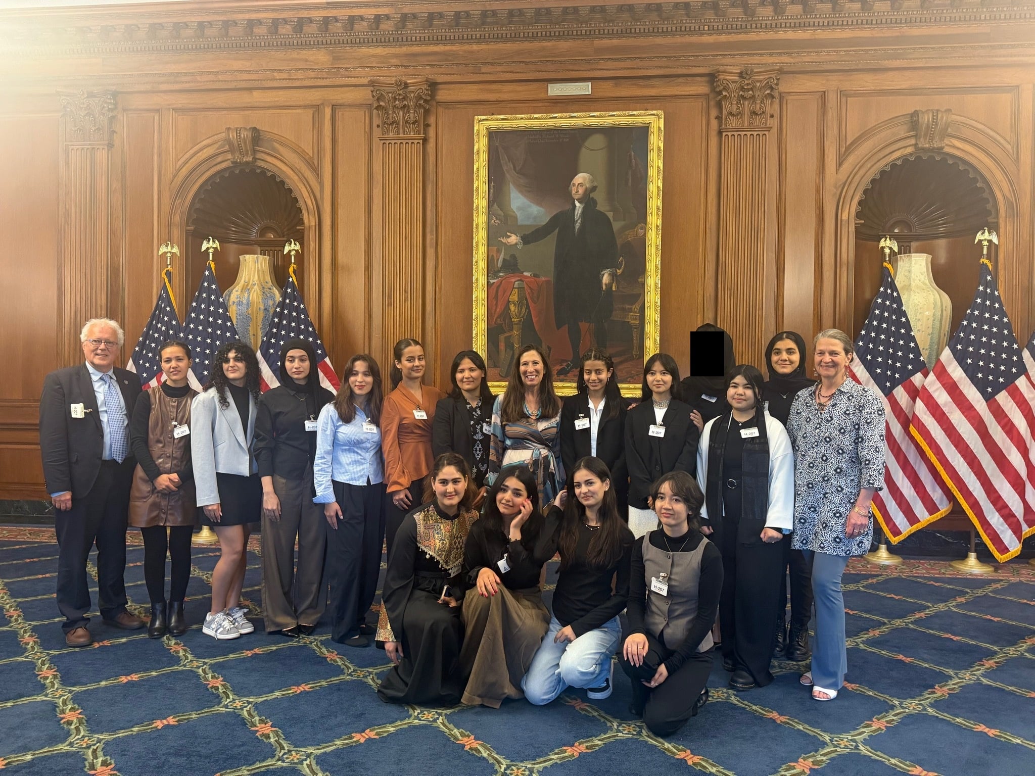 ASRF students standing with Representative Theresa Leger Fernandez in a wood-paneled Capitol room with United States flags behind them