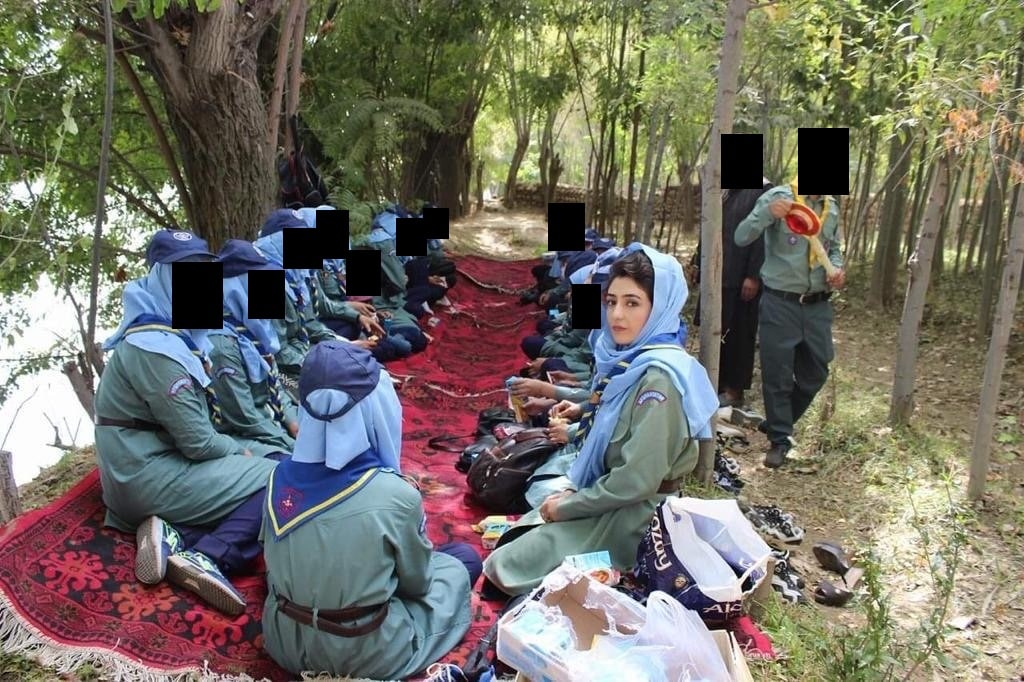 Afghan scouts in uniform sitting on red carpets spread out under trees at an outdoor gathering