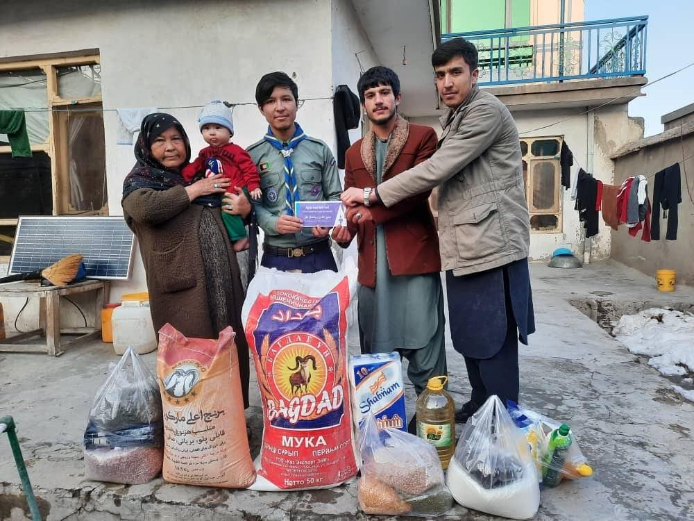 Scouts delivering sacks of flour, cooking oil and other food staples to a family in a courtyard