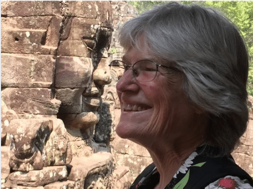 Cindy Piatt smiling in profile in front of a carved stone face at an ancient temple