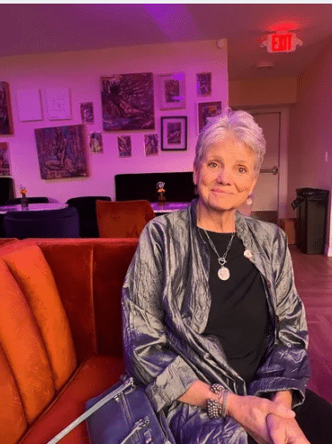 Cynthia Shore seated in a gallery with artwork on the walls behind her